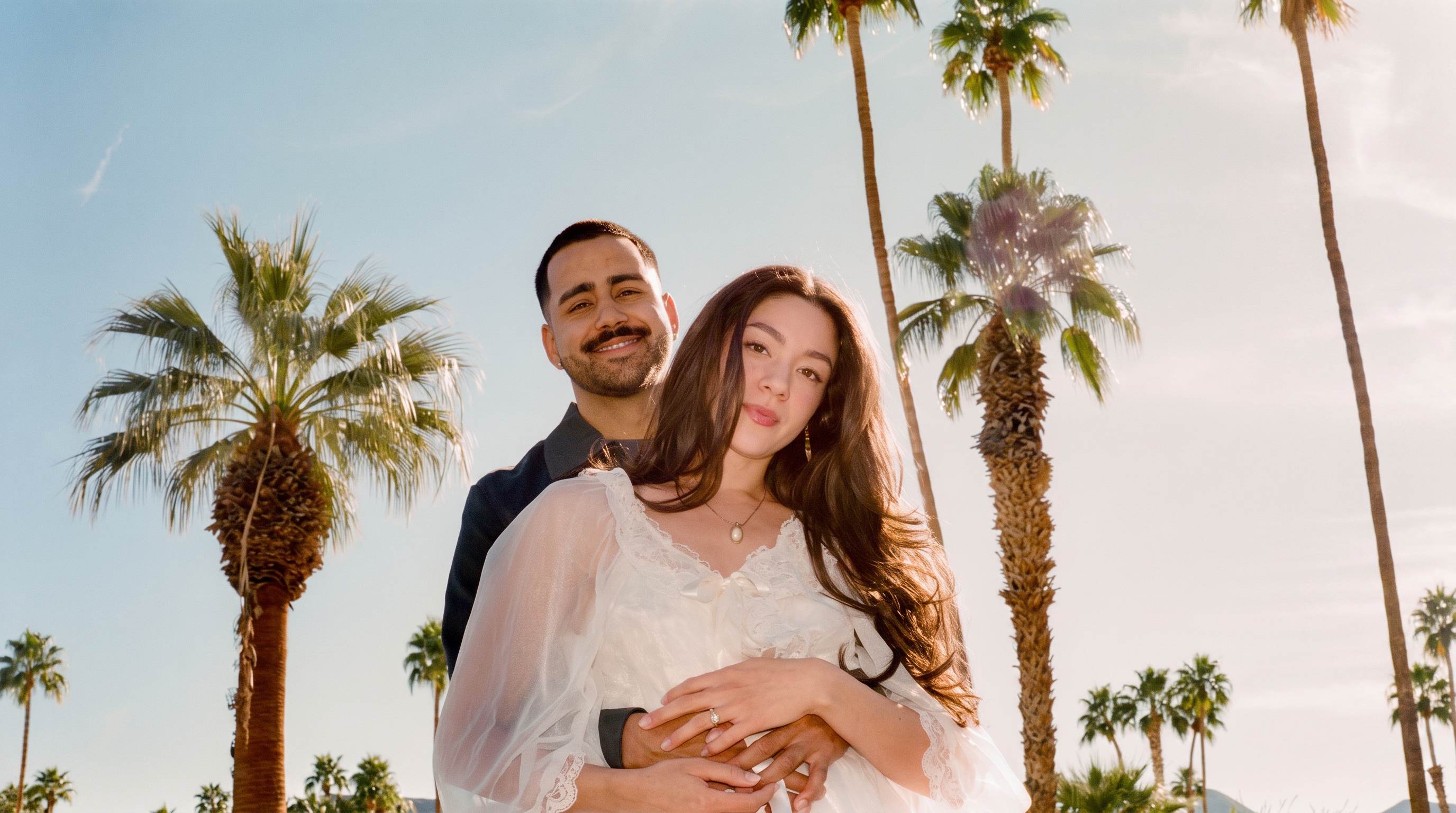 Stephanie and Johan embracing among tall palm trees in the La Quinta desert sunlight